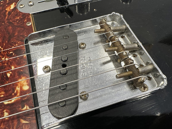 Close-up of Fender Telecaster guitar bridge and single-coil pickup with metal saddles and strings on black guitar body