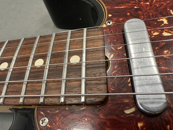 Close-up of vintage electric guitar fretboard with dot inlays, metal frets, metal single-coil pickup, and tortoiseshell pickguard.