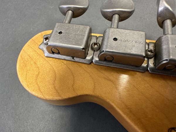 Close-up of vintage guitar tuning machines on natural wood headstock with visible metal hardware and screws