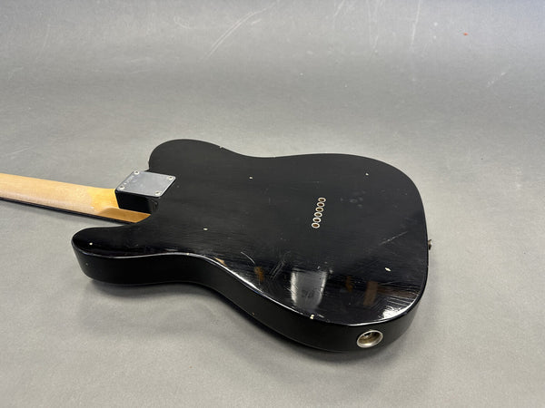 Black electric guitar body showing rear side with six string ferrules and metal neck plate on gray background