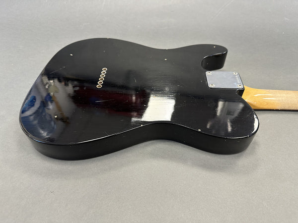 Black electric guitar body with light wood neck and visible wear scratches on gray background