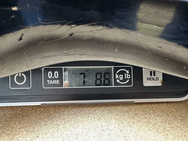 Digital scale display showing guitar weight of 7 pounds 8.6 ounces on a wooden surface at Coffee House Guitars.