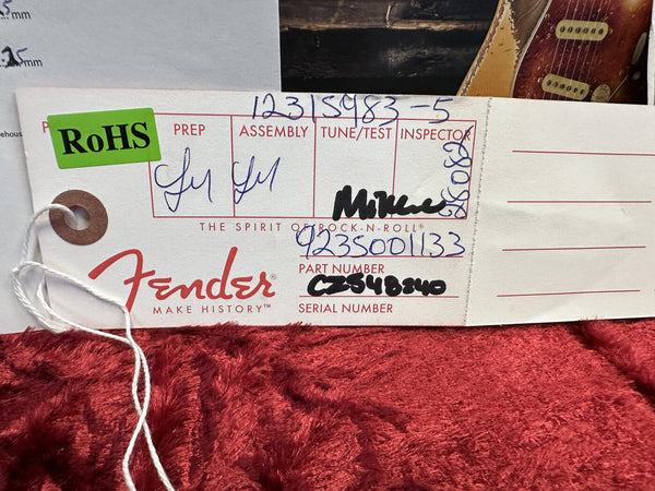 Fender guitar inspection tag with RoHS sticker, handwritten assembly and inspection details, part number 9235001133, serial number CZ548240, on red textured background.