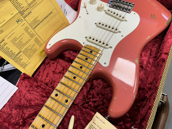 Close-up of vintage pink Fender Stratocaster guitar with maple fretboard and white pickguard resting in red plush-lined guitar case with original paperwork and specifications sheet from Coffee House Guitars.