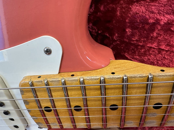 Close-up of pink electric guitar body with white pickguard and maple fretboard showing metal frets and steel strings on red textured background
