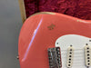 Close-up of coral pink electric guitar body with worn paint and white pickguard resting in vintage red velvet-lined guitar case