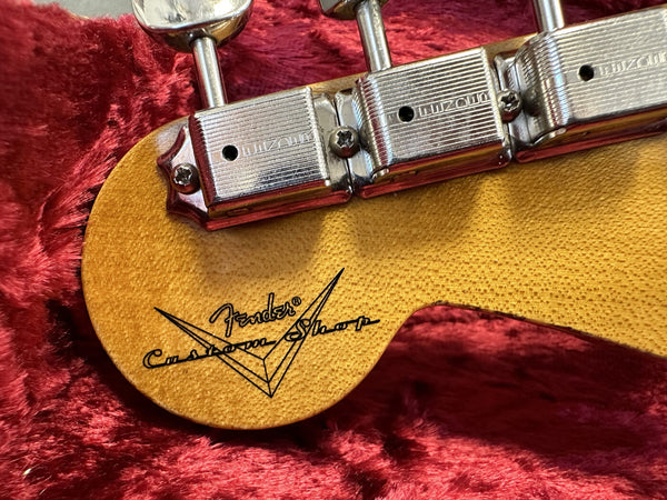 Close-up of Fender Custom Shop logo on vintage guitar headstock with vintage tuners against red plush background