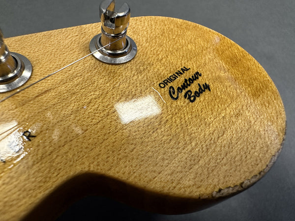Close-up of guitar headstock with "Original Contour Body" decal, natural wood finish, and metal tuning pegs.