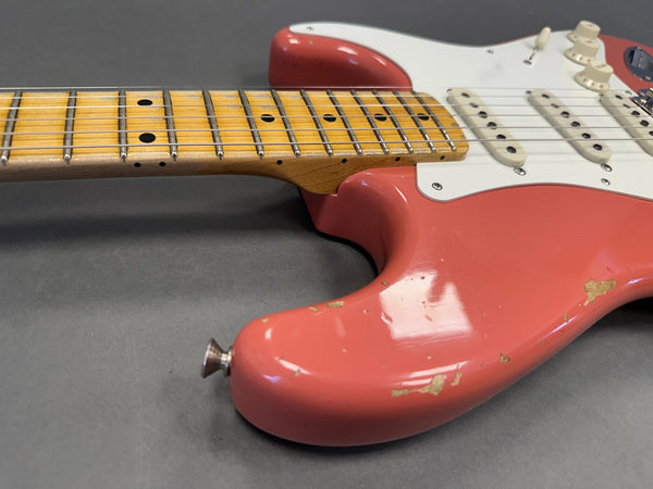 Close-up of worn red electric guitar body with white pickguard and maple fretboard on gray background