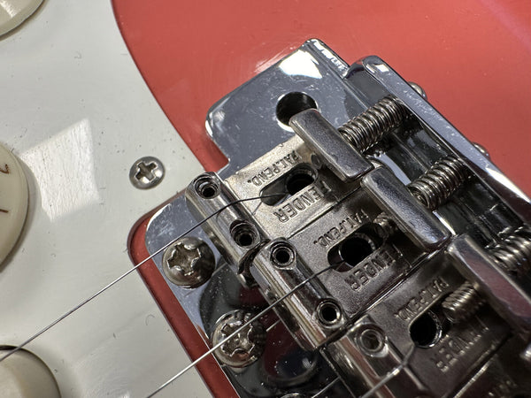 Close-up of chrome Fender vintage-style guitar bridge and saddles on a red and white electric guitar body with strings and adjustment screws visible