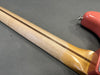 Close-up of natural wood guitar neck with skunk stripe detail and part of coral-colored guitar body on gray background