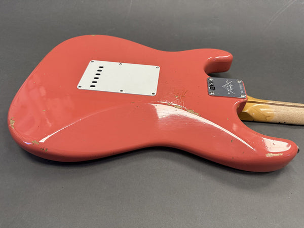 Back side of a coral red electric guitar with visible wear and scratches on the body and a light wood neck, lying on a gray surface.