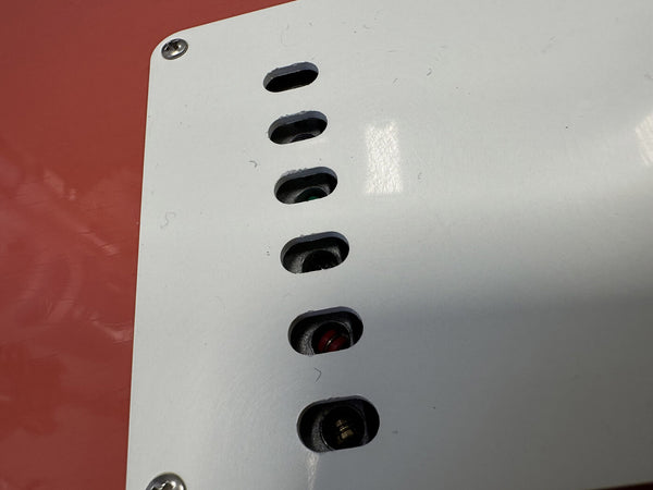 Close-up of white guitar tremolo backplate showing six string ferrules on a red electric guitar body