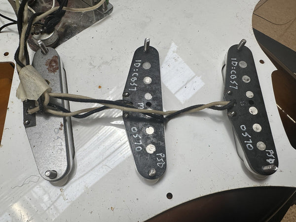 Vintage single coil pickups mounted on white guitar pickguard with visible wiring and identification markings.