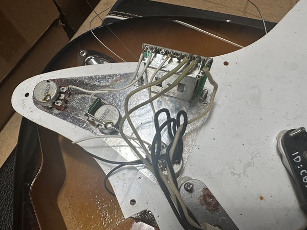 Close-up of guitar pickguard wiring and potentiometers showing internal electronics and components on sunburst electric guitar body