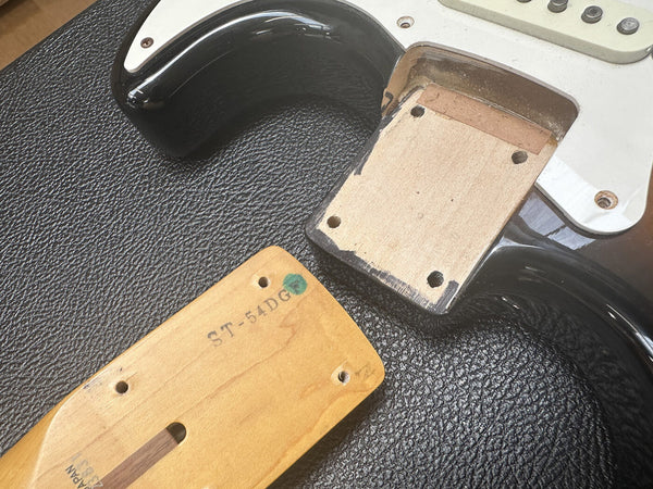 Close-up of disassembled electric guitar body and neck with stamped model number ST-54DG on neck heel, showing neck pocket and wood grain.