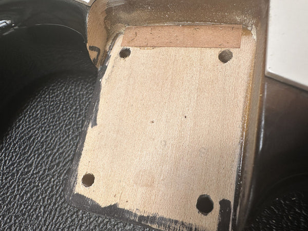Close-up of guitar neck pocket showing wood grain and screw holes for neck attachment on a black electric guitar body