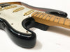 Close-up of black electric guitar body and maple neck with white pickguard, showing guitar strings and pickups on white background.