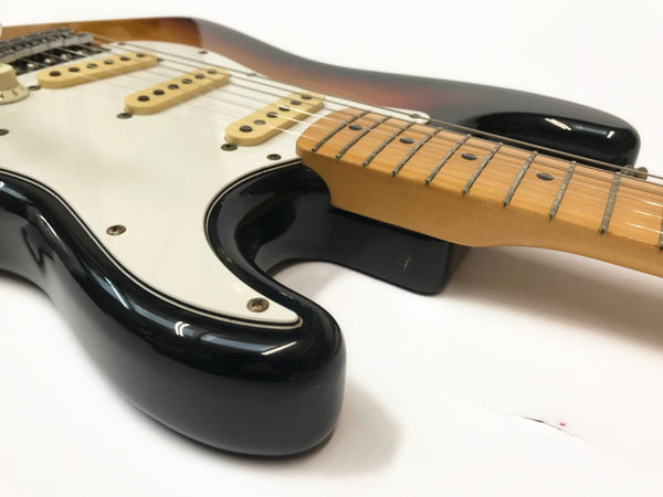 Close-up of black electric guitar body and maple neck with white pickguard, showing guitar strings and pickups on white background.