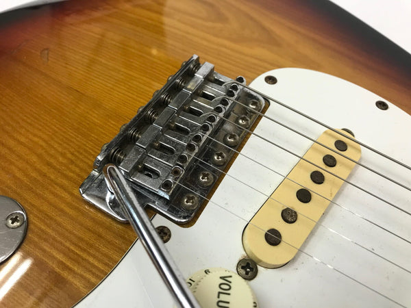 Close-up of electric guitar bridge, single-coil pickup, and volume knob on sunburst finish guitar body with white pickguard and vibrato arm.