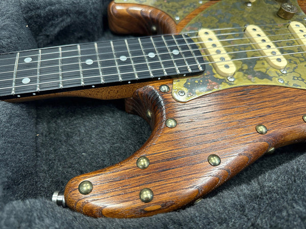 Close-up of vintage electric guitar with wooden body, aged brass hardware, and black fretboard with dot inlays resting in a black plush guitar case.