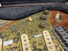 Close-up of vintage electric guitar with unique green patina pickguard, cream single-coil pickups, and aged metal control knobs in guitar case