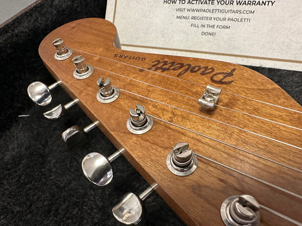 Close-up of Paoletti guitar headstock with tuning pegs and warranty activation instructions in the background