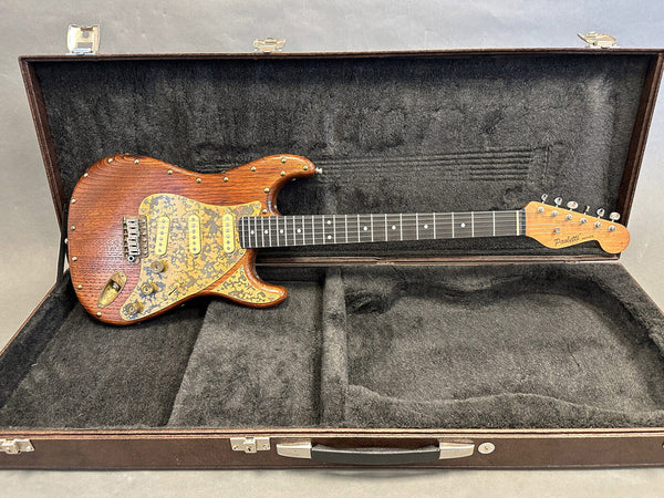 Paoletti electric guitar with wooden finish and gold pickguard in open black plush-lined hard case on gray background.