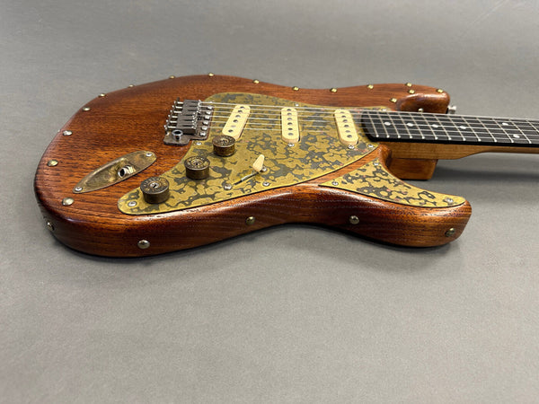 Electric guitar with custom wood body and brass hardware, three single-coil pickups, and decorative brass pickguard with knob controls on gray background