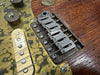 Close-up of vintage electric guitar bridge, strings, cream single-coil pickup, and aged brass pickguard on wooden guitar body