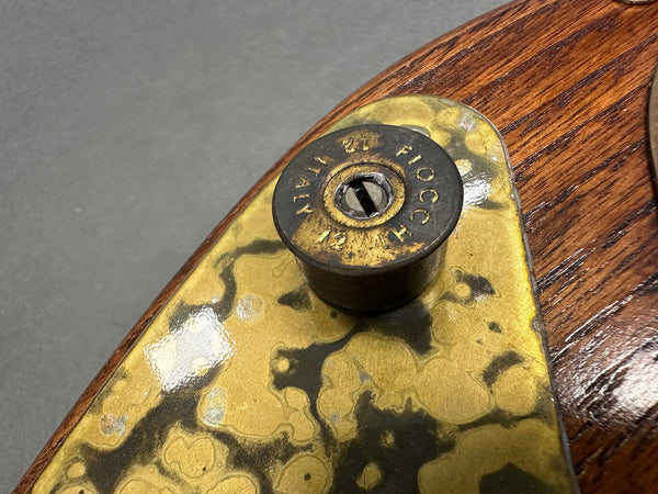 Close-up of Fiocchi 12 gauge shotgun shell casing used as a vintage guitar strap button on a wooden electric guitar with brass pickguard plating.