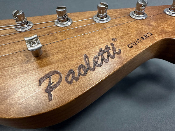 Close-up of Paoletti Guitars wooden guitar headstock with metal tuning pegs and strings on gray background