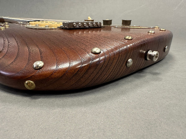 Close-up angled view of dark wood electric guitar body with silver rivets and metal strap button on gray background