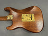 Back of electric guitar with natural wood finish and textured yellow metal plates on gray background