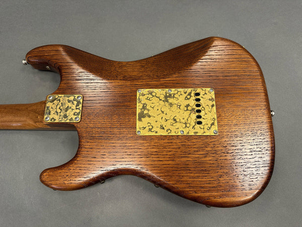 Back of electric guitar with natural wood finish and textured yellow metal plates on gray background