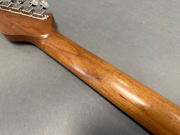 Close-up of smooth wooden guitar neck and chrome tuning pegs on gray background