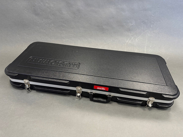 Black hard shell guitar case with Music Man logo embossed on top, silver latches, and a sturdy handle for electric guitar protection and transport.