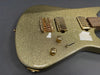 Close-up of gold sparkle electric guitar body with gold hardware, humbucker pickups, bridge, control knobs, and toggle switch on dark background