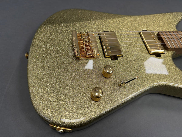 Close-up of gold sparkle electric guitar body with gold hardware, humbucker pickups, bridge, control knobs, and toggle switch on dark background