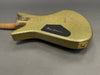 Back side of gold sparkle electric guitar body with black control cavity cover and wooden neck visible on gray background