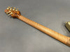 Back view of electric guitar neck with flamed maple wood and gold tuning pegs on gray background