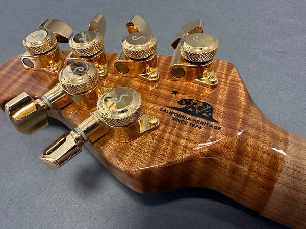 Close-up of guitar headstock with gold tuning pegs and California Heritage Since 1974 logo on glossy wood finish
