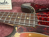 Close-up of vintage Fender Precision Bass guitar fretboard and pickguard showing wear and aged tortoiseshell pattern in plush case