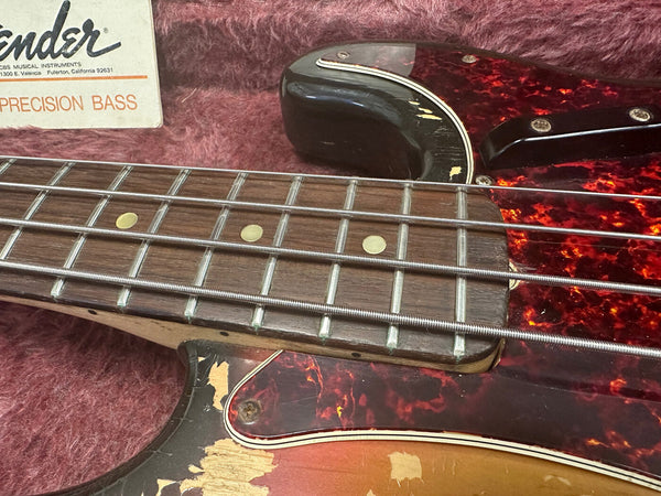 Close-up of vintage Fender Precision Bass guitar fretboard and pickguard showing wear and aged tortoiseshell pattern in plush case