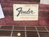 Fender Precision Bass owner's manual resting on red plush guitar case lining above bass guitar fretboard with metal strings and dot inlays