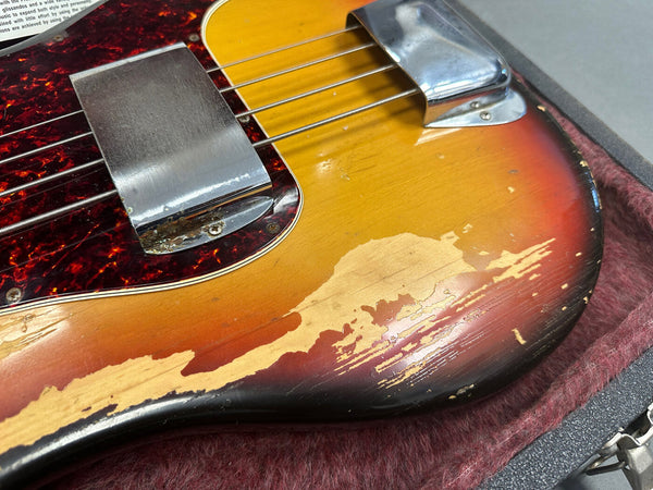 Close-up of vintage sunburst electric guitar body with worn and chipped finish, tortoiseshell pickguard, and metal pickup covers resting in a padded guitar case