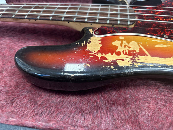 Close-up of worn sunburst finish on electric guitar body showing faded paint and scratches, vintage style electric guitar detail on red fabric background