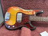 Vintage sunburst electric bass guitar with tortoiseshell pickguard and chrome pickup cover, showing worn and relic finish on body, resting on plush maroon guitar case interior.