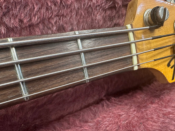 Close-up of a Fender bass guitar maple neck with rosewood fretboard and metal frets on a purple plush background