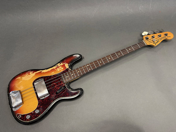 Vintage Fender Precision Bass with sunburst finish and tortoiseshell pickguard, showing wear and aging on body and hardware, with rosewood fingerboard and four tuning pegs on the natural wood headstock.